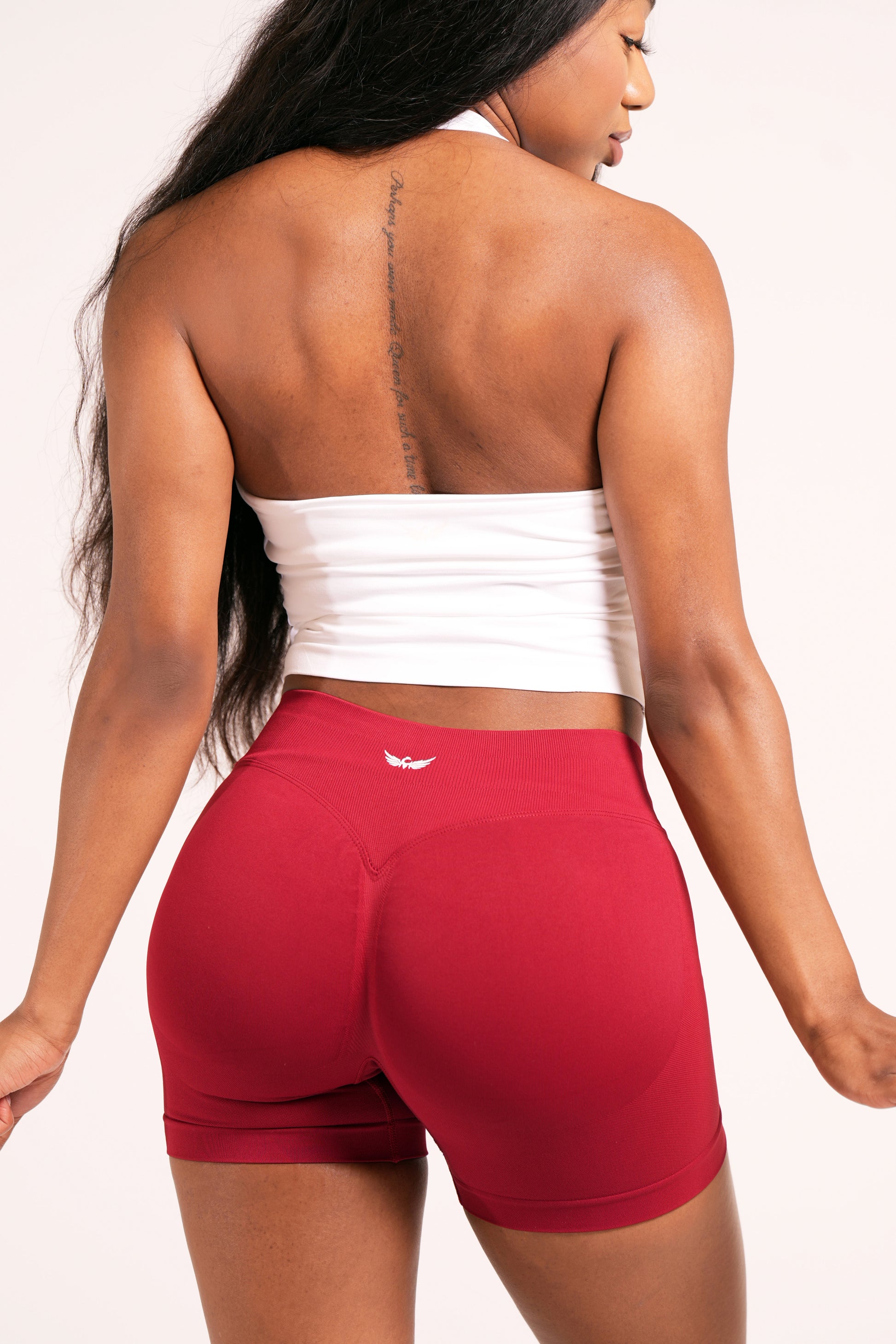 Person wearing a white halter top and crimson red biker shorts on a plain white background