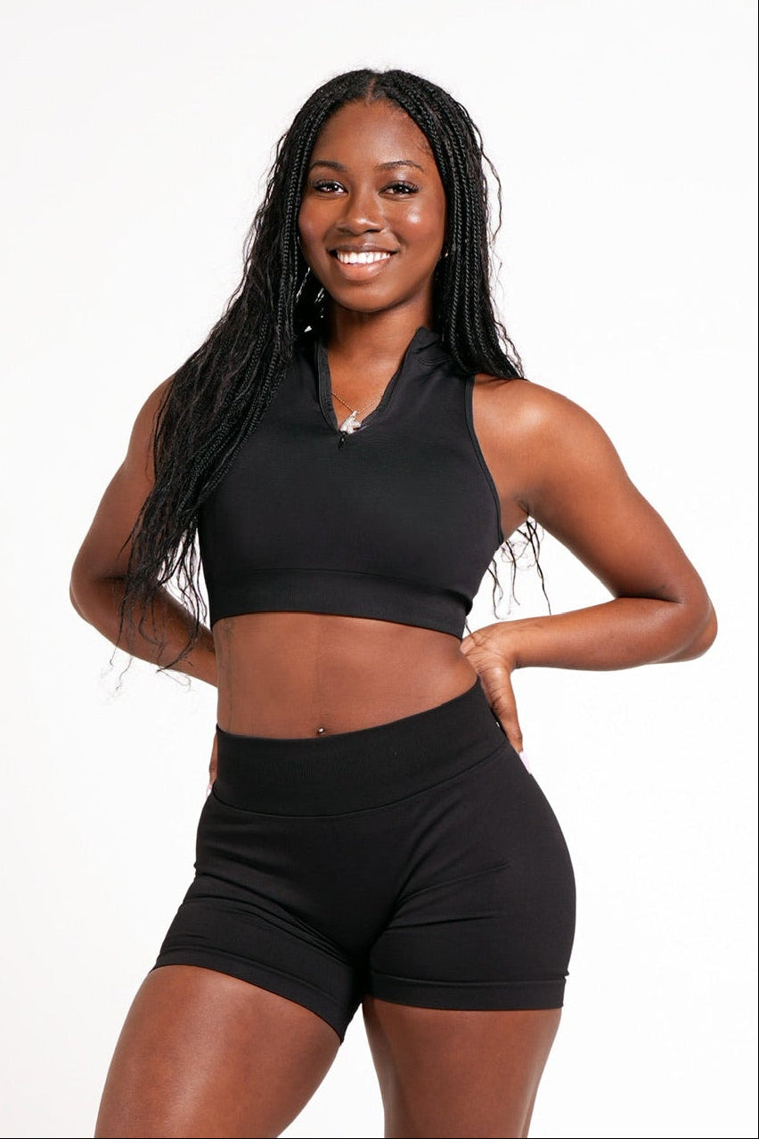 Woman wearing an athletic black crop top with a high neck, quarter zip feature in front of a plain white background