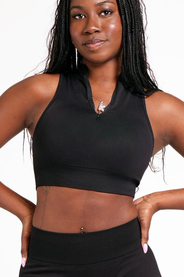 Woman wearing an athletic black crop top with a high neck, quarter zip feature in front of a plain white background