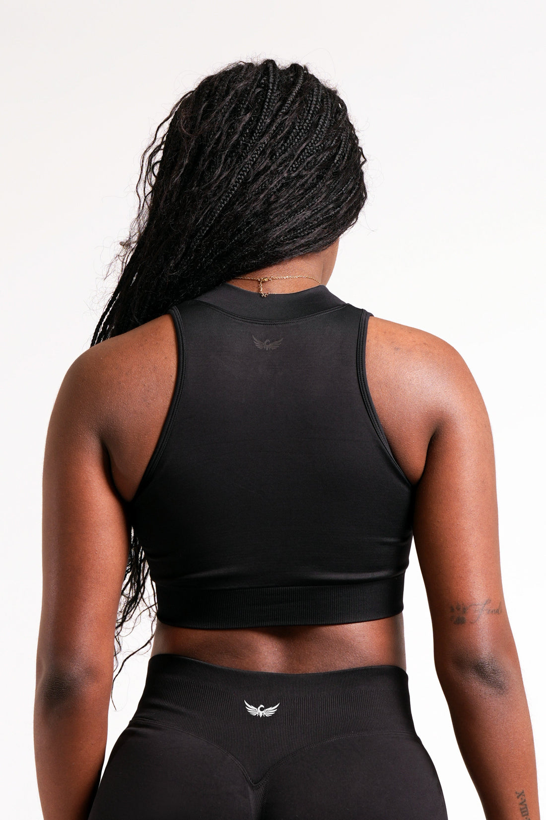 Woman wearing an athletic black crop top with a high neck, quarter zip feature in front of a plain white background