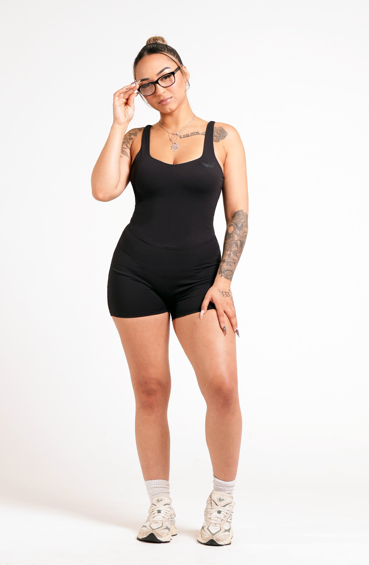 Woman wearing a black conquered romper with a tone on tone image logo on a white background