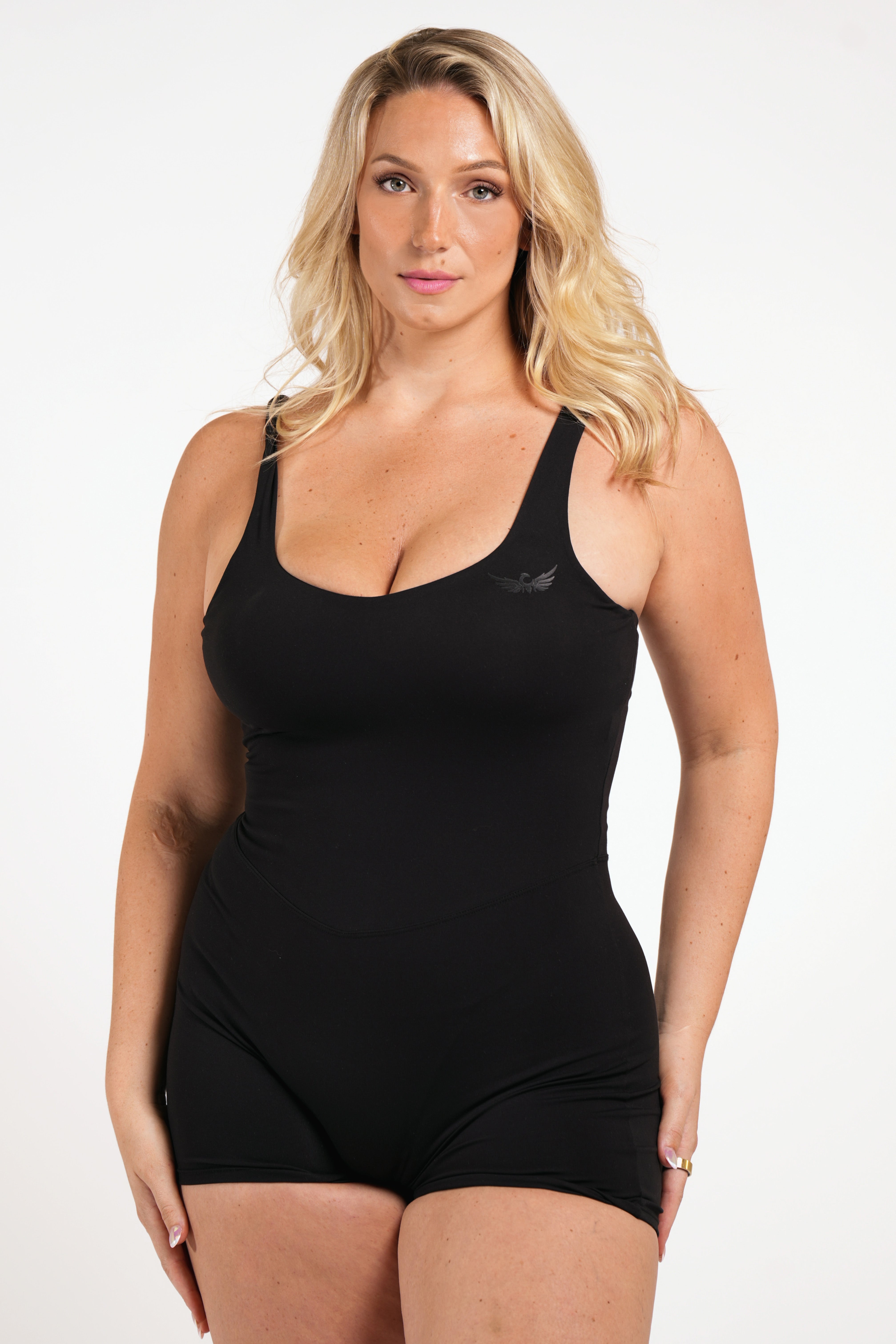 Woman wearing a black conquered romper with a tone on tone image logo on a white background
