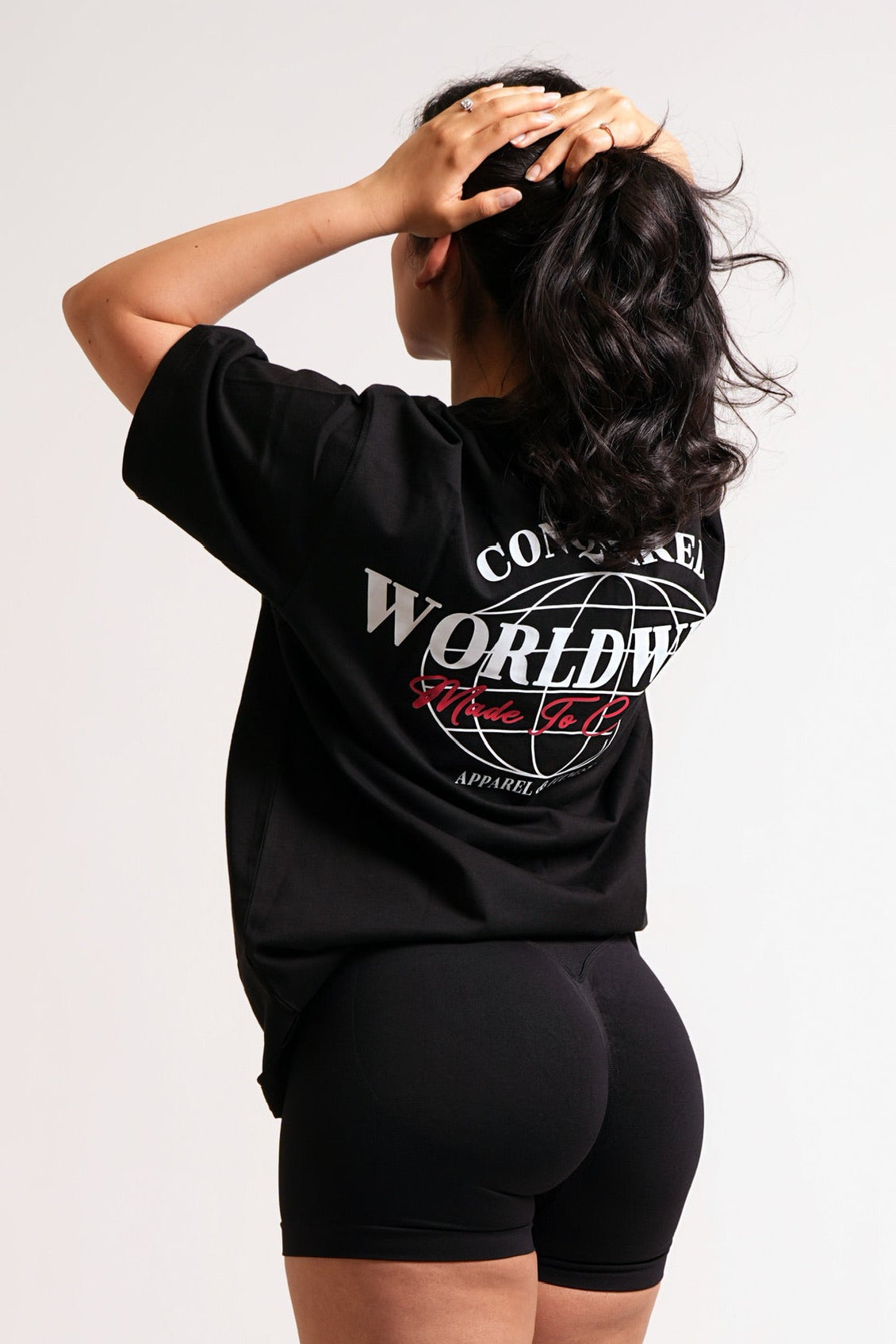 Girl wearing a short sleeve black oversized t-shirt with a graphic design that reads "CONQUERED WORLDWIDE" in white and "Made To Conquer" in red on a plain white background