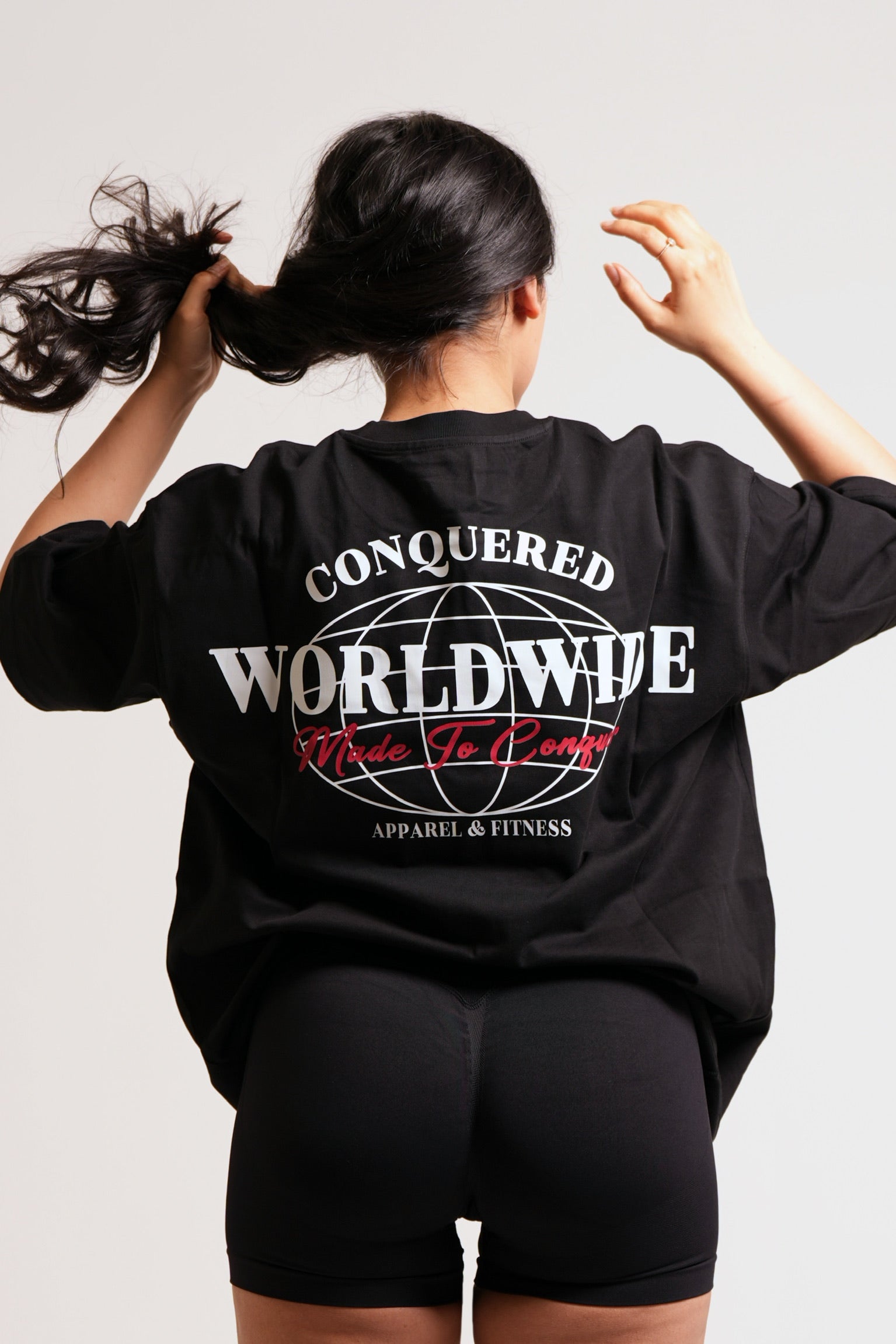 Person wearing a black hoodie with 'Conquered Worldwide Apparel & Fitness' in white text and 'Made To Conquer' in red text on the back.