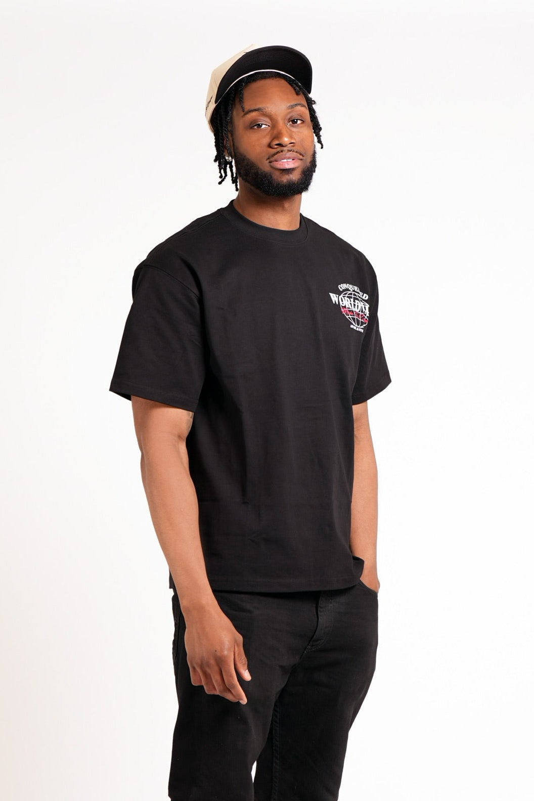 Man wearing a short sleeve, black t-shirt with a CONQUERED graphic logo on the upper left side standing in front of a white background